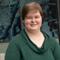 A woman with short brown hair wearing a green cowel neck sweater.